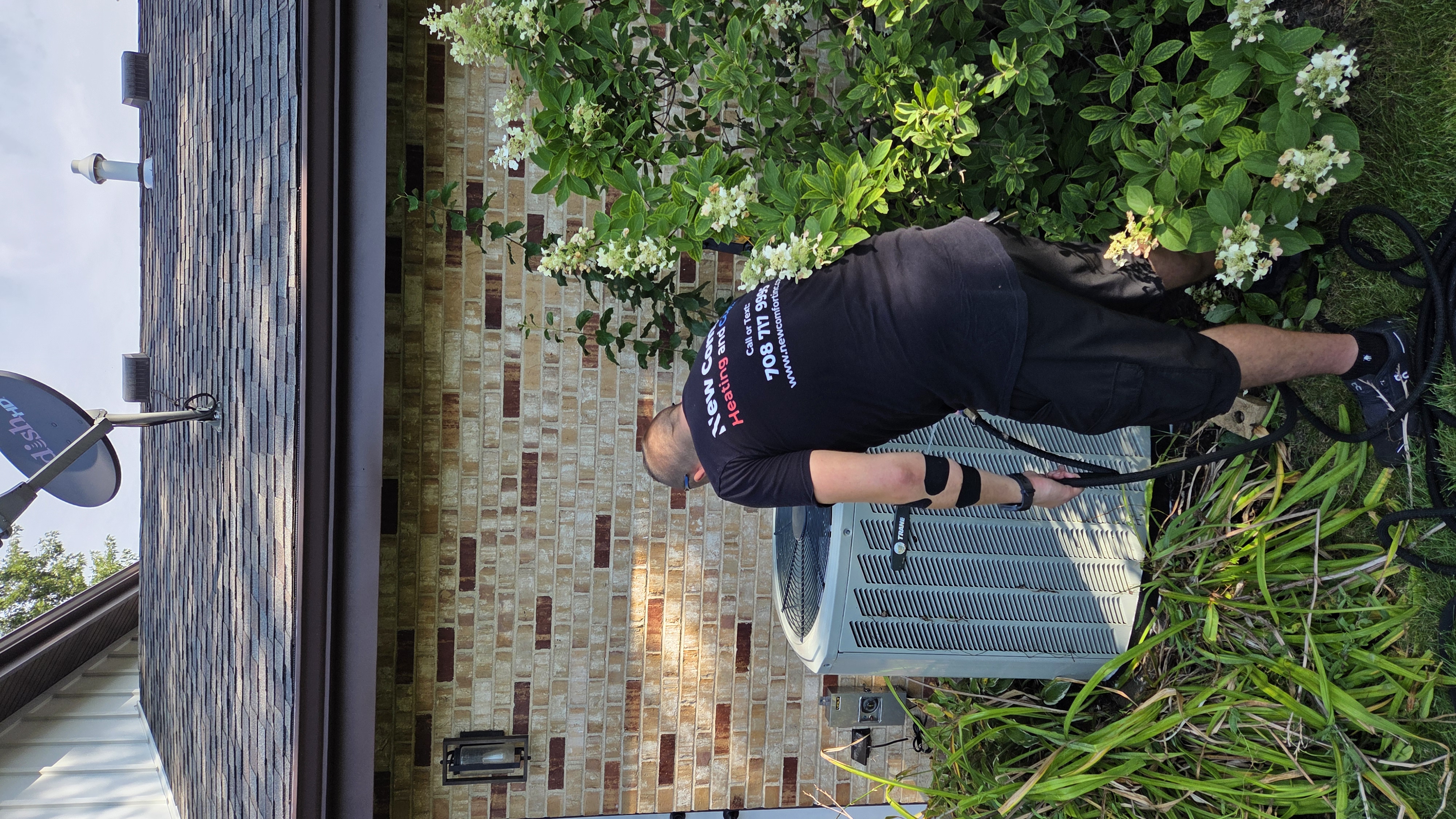 New Comfort technician servicing an outdoor air conditioner beside a brick home - HVAC services Indian Head Park IL