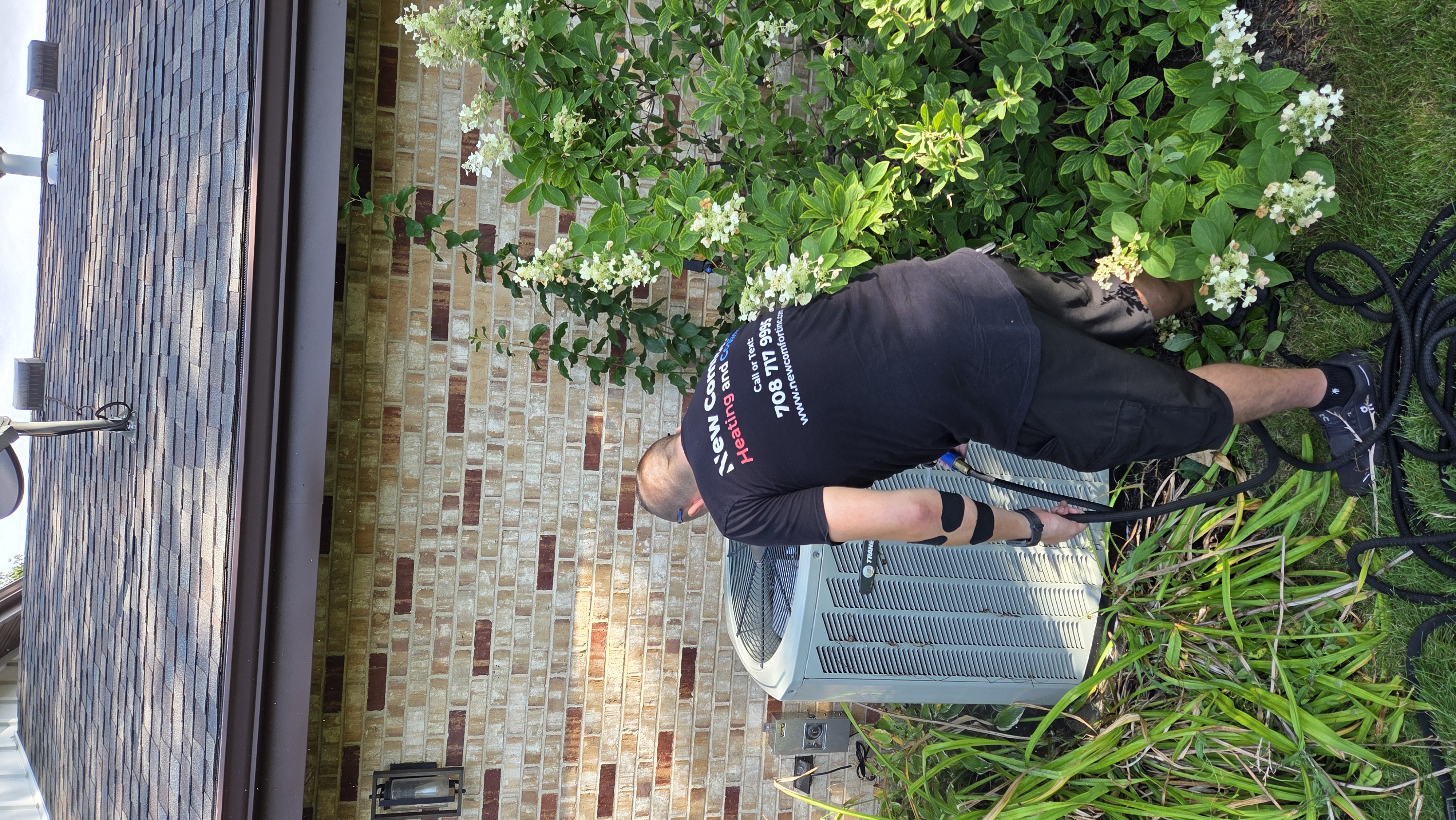 New Comfort technician rinsing an outdoor AC condenser coil during a seasonal tune-up