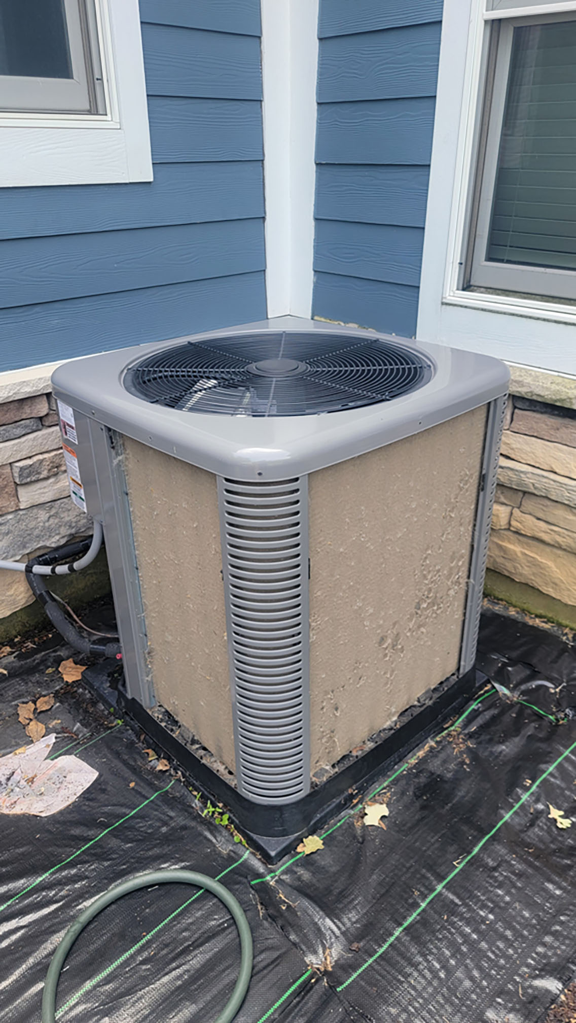 Outdoor AC condenser with coil fins covered in cottonwood and debris before cleaning