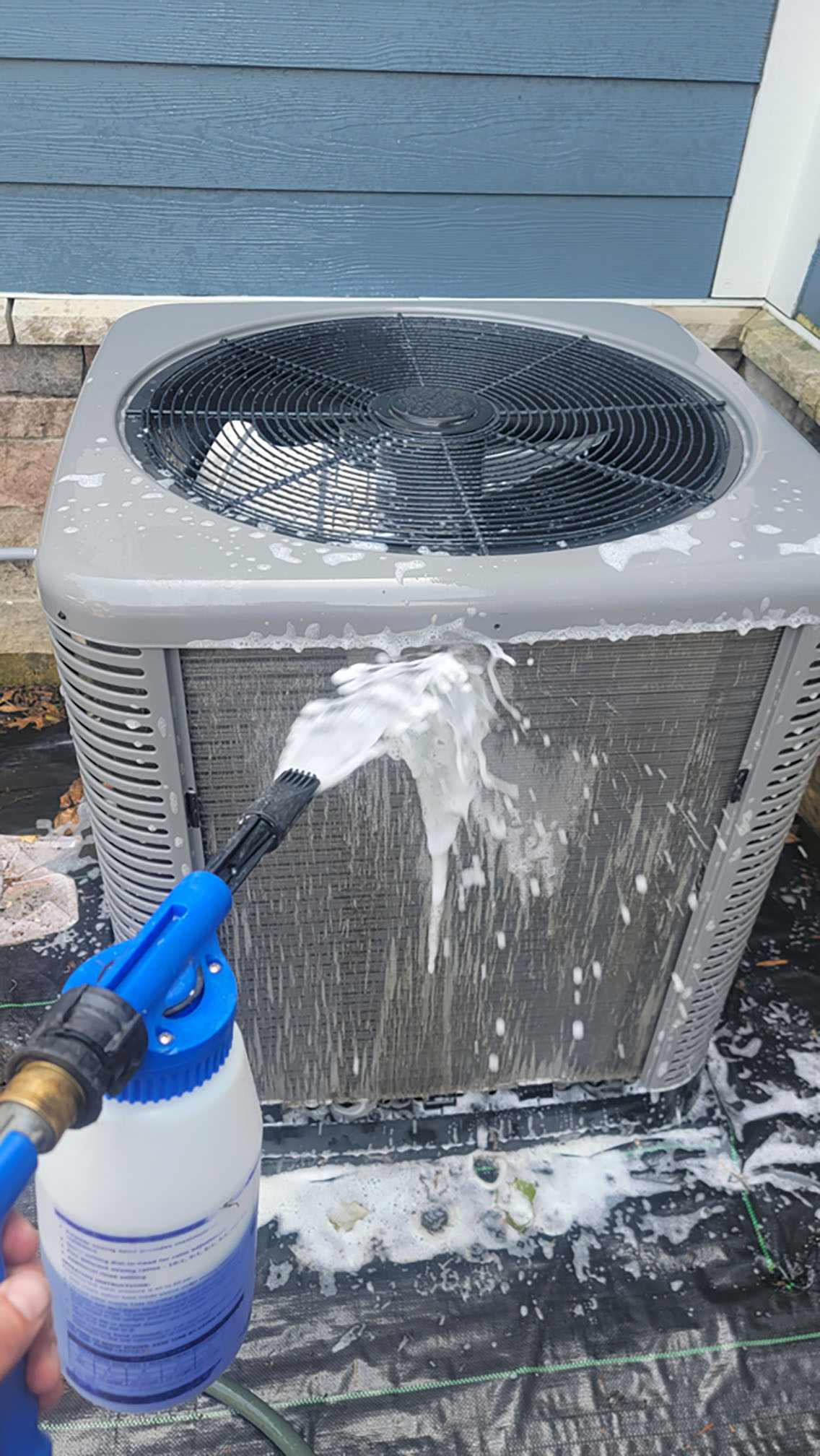 Technician applying coil cleaner to an outdoor AC condenser during a maintenance visit